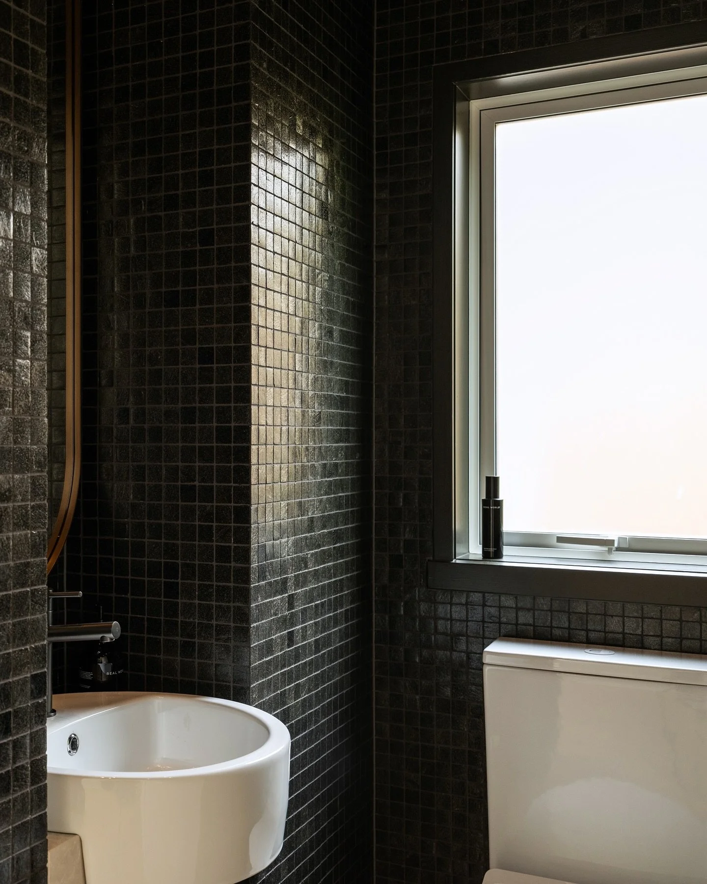 We created a bit of drama in this tiny powder room by wrapping it in these delicious liquorice coloured glass tiles. The door and window frame were painted to match.

Click the link in our profile to see more in our Latest Project and our Latest Blog