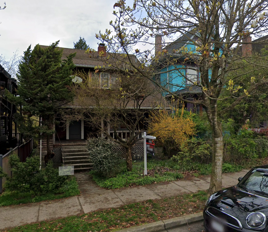 A residential house with trees and plants in front, stairs leading up to the porch, and a black car parked on the street.