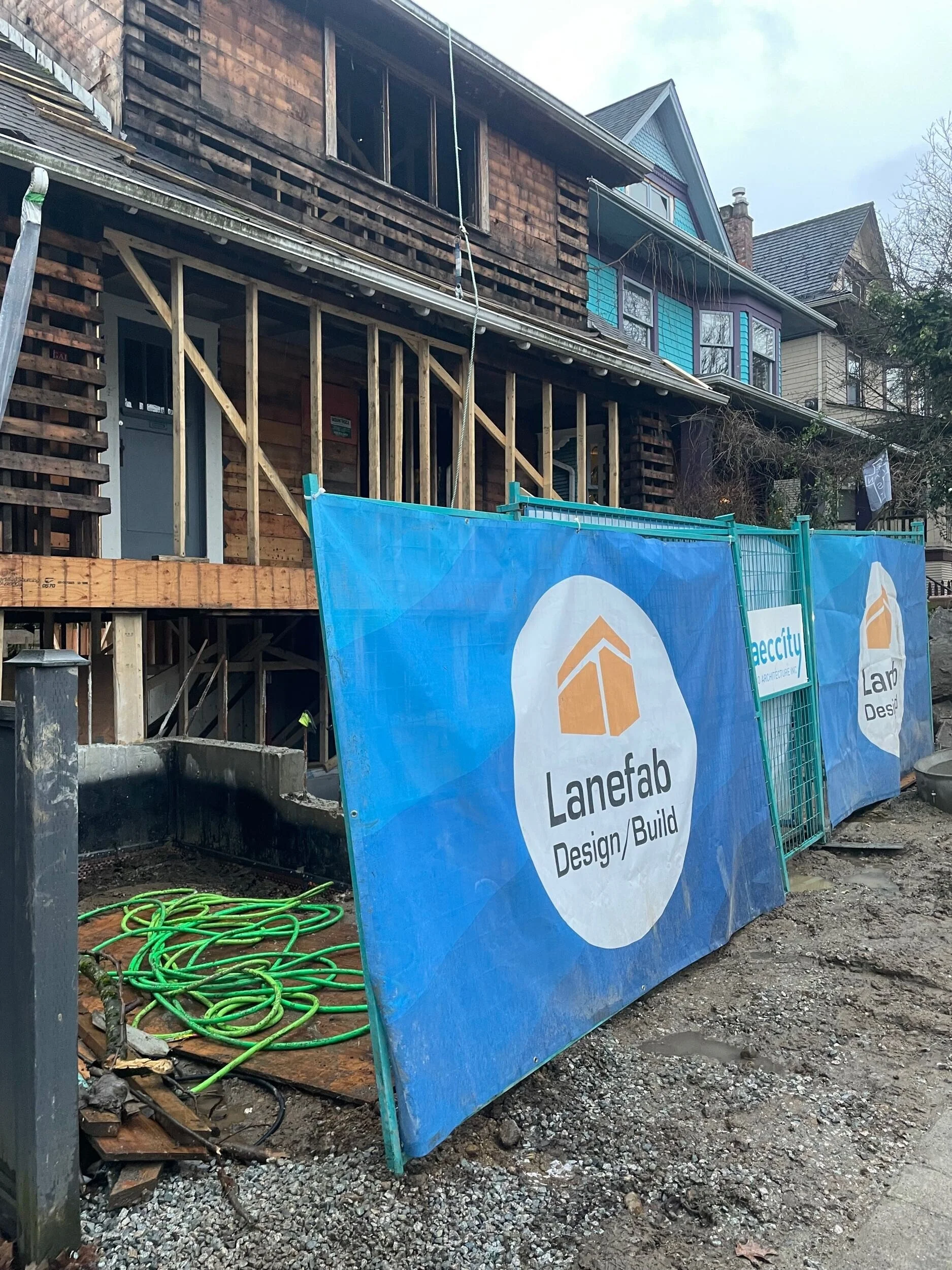 Construction site in front of a partially renovated multi-story house with signs for Lanefab Design/Build.