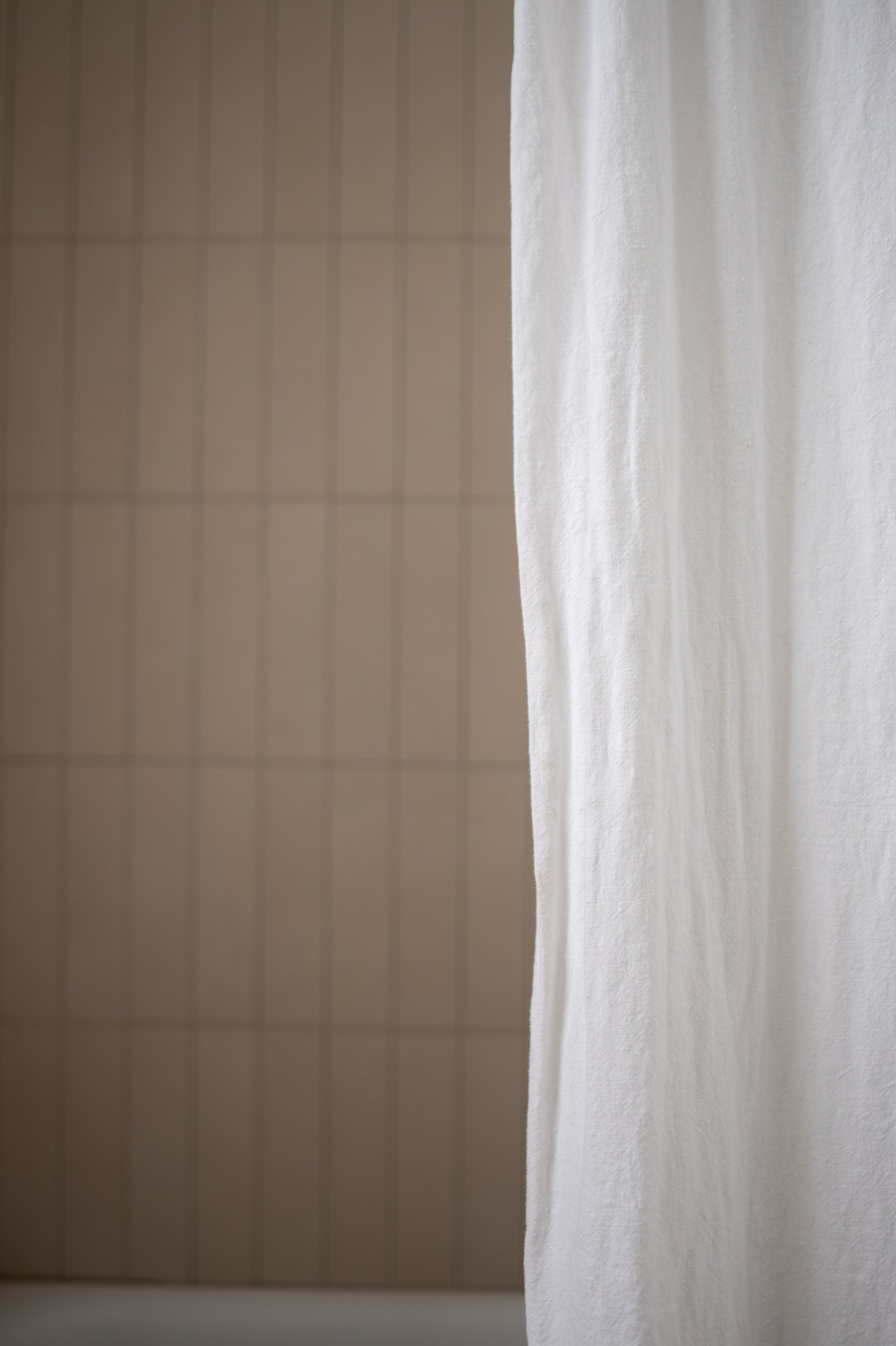 Linen shower curtain in front of modern tan shower tile in vertical rows