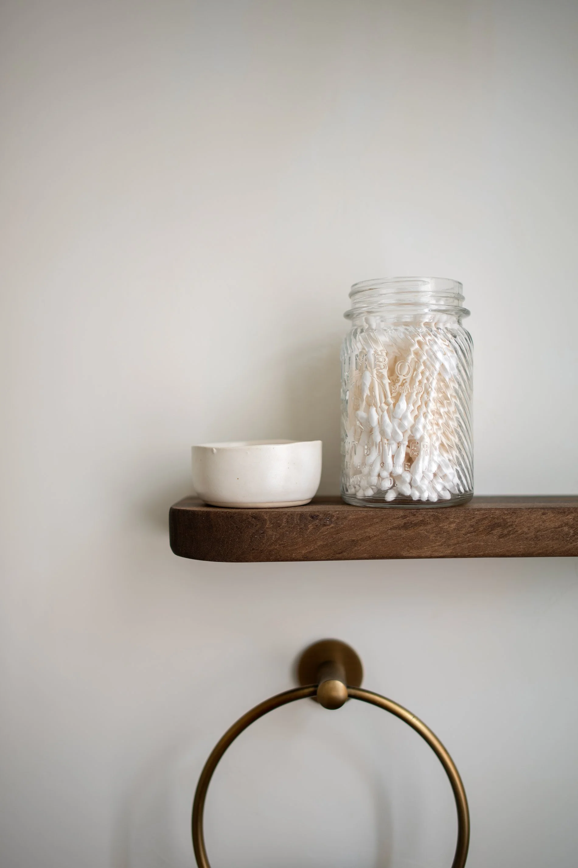 Vintage textured glass jar with q-tips in it and rustic wabi-sabi ceramic bowl on a curved wooden shelf