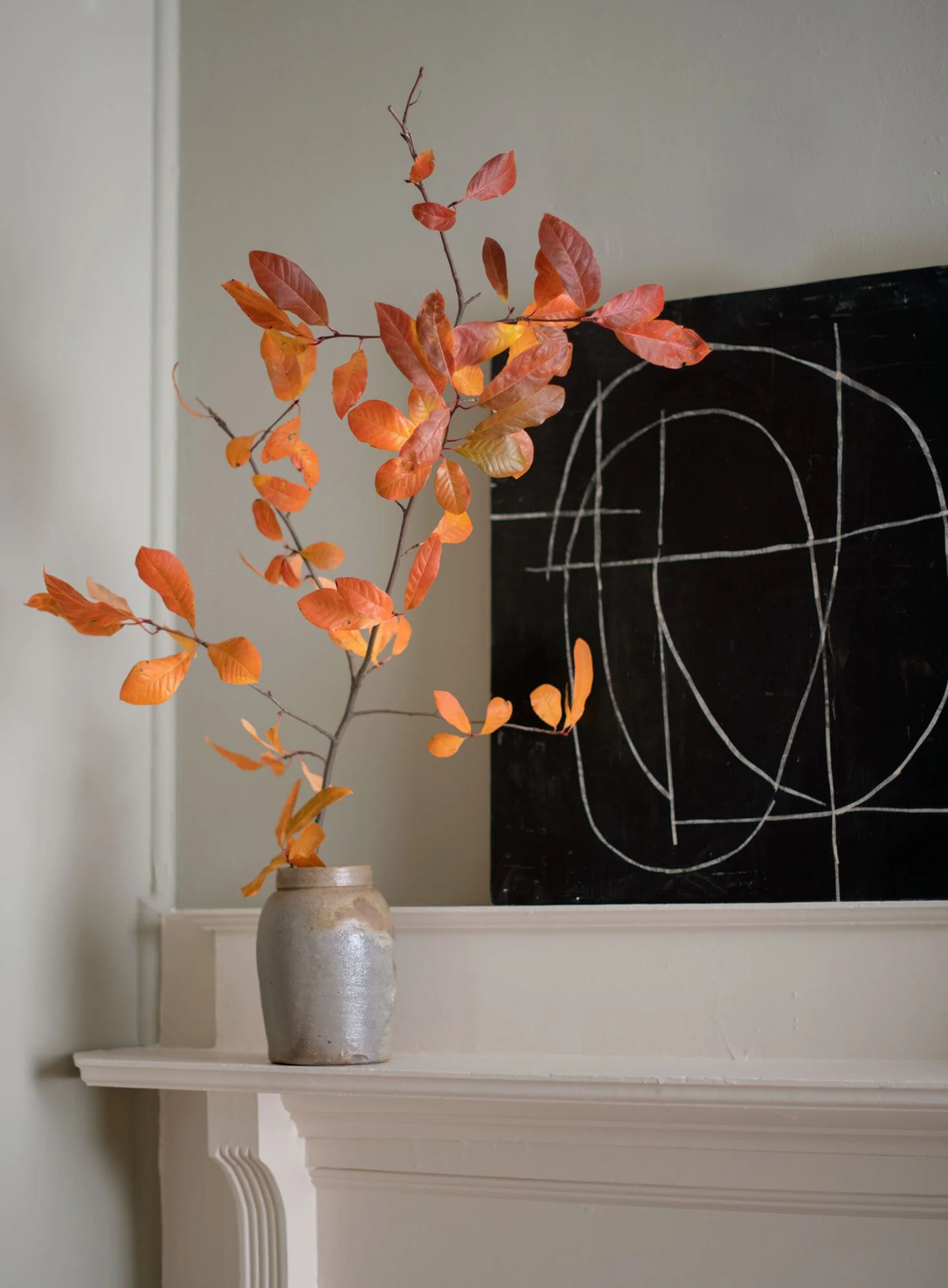 historic townhouse mantel with autumn fall branches in antique ceramic vase with abstract art in the background