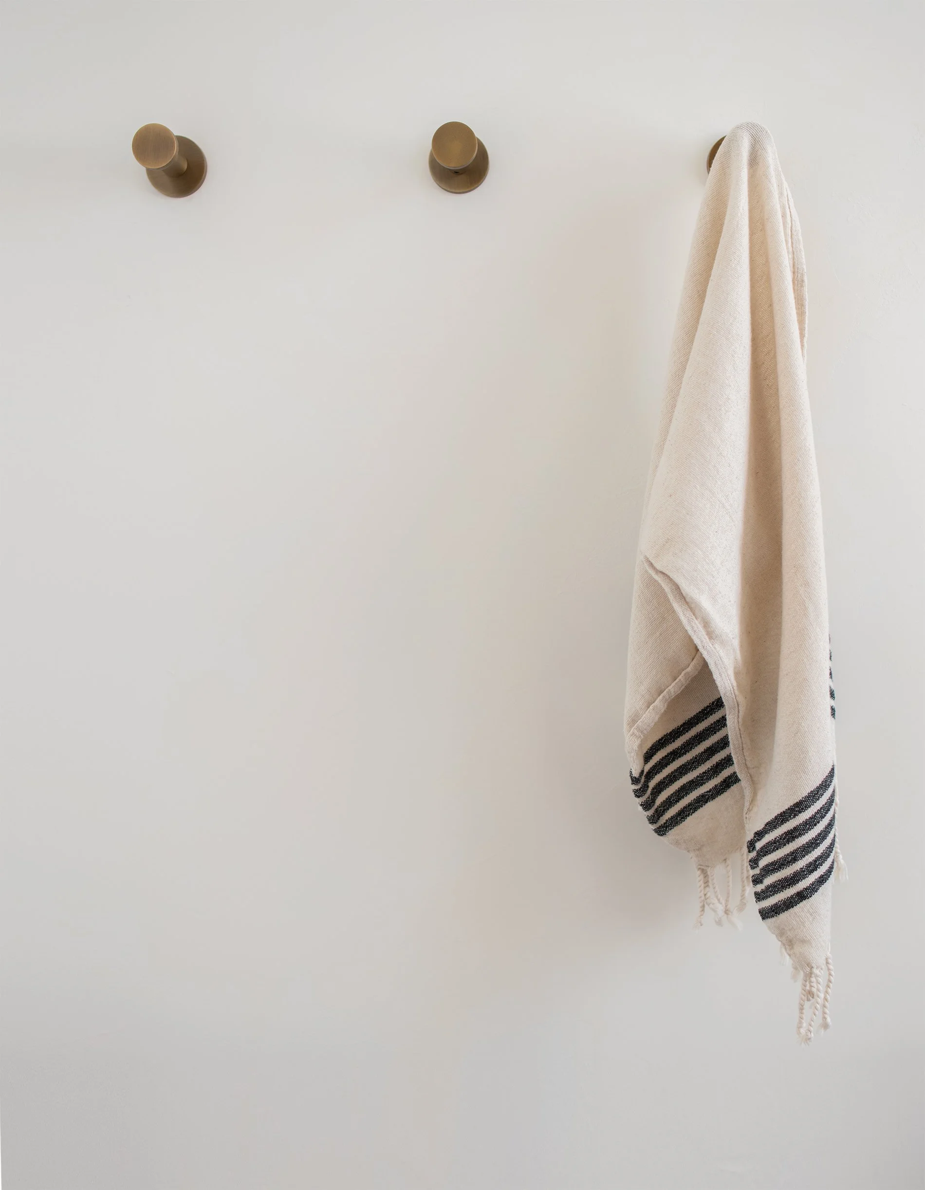 Striped Turkish towel hanging on brass hook in modern bathroom with roman clay textured wall
