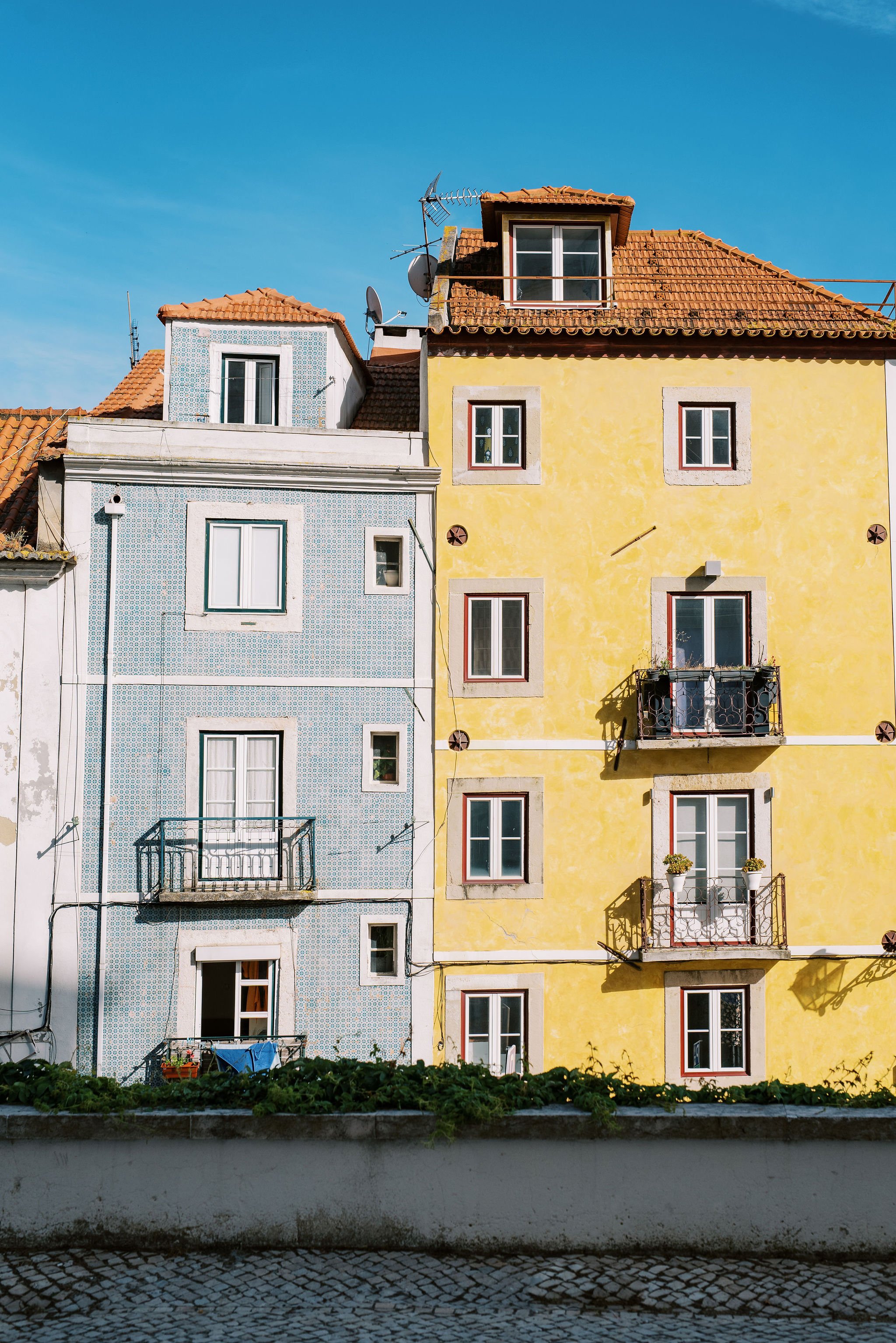 Two buildings next to each other in the city of Lisbon, one with blue and white tiles, the other with yellow walls, showing the colorful architecture of Portugal's capital