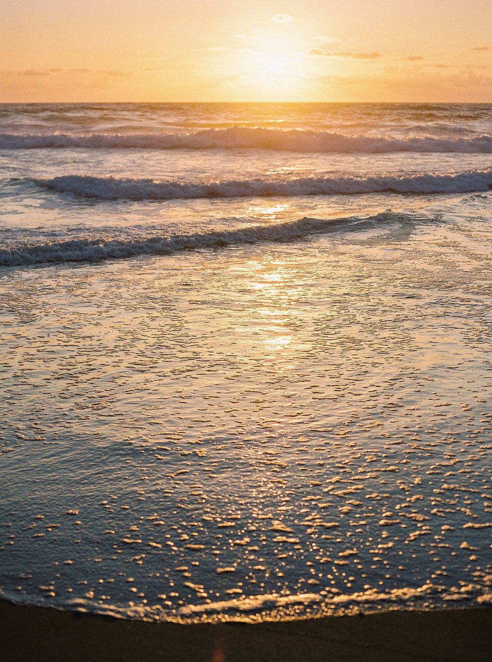 Golden hour above the ocean, painting the slightly wavy water orange and yellow