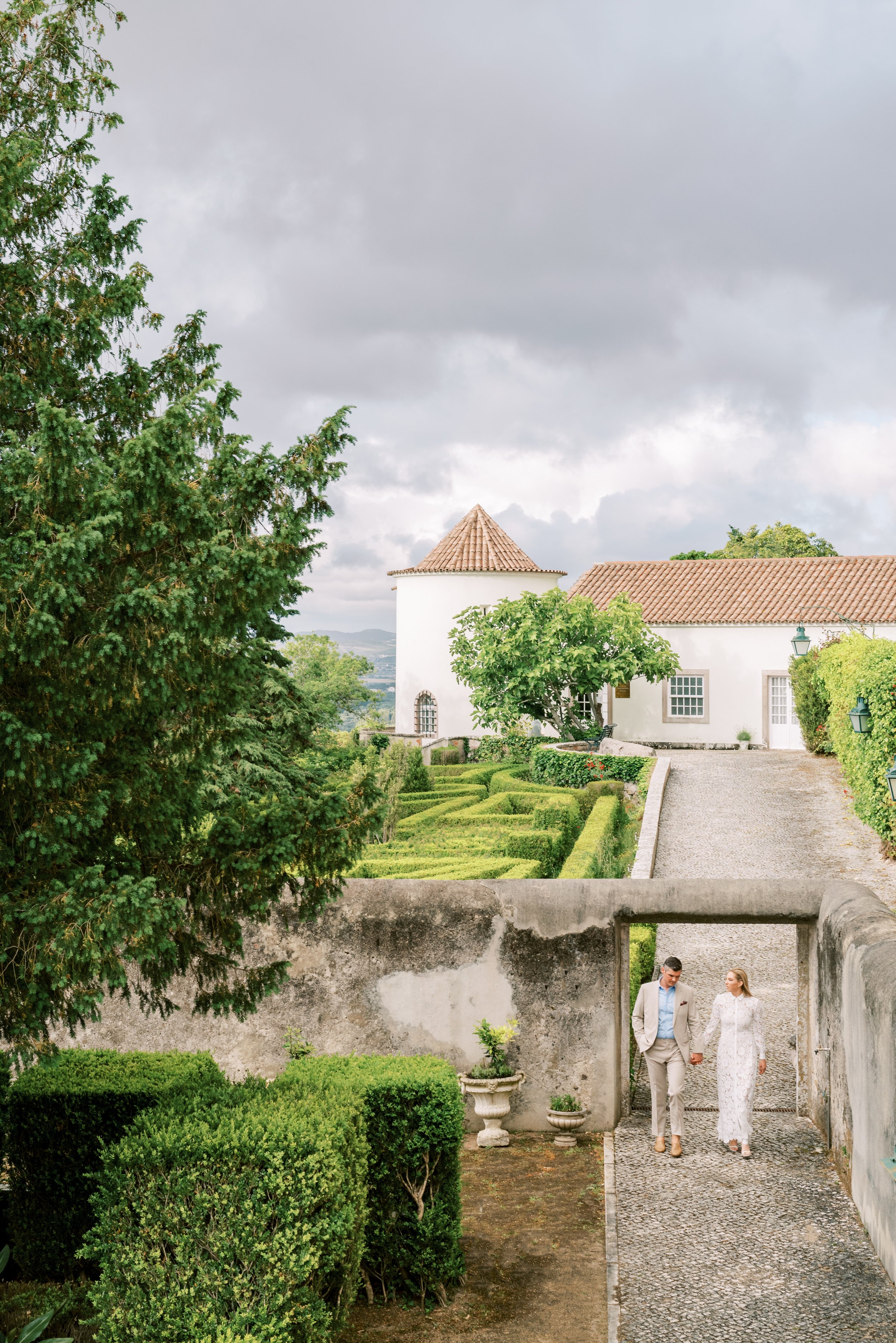 Bride and groom walking through a small arch in the gardens behind Palácio de Seteais with a glamour and a touch of Portuguese rural feeling 