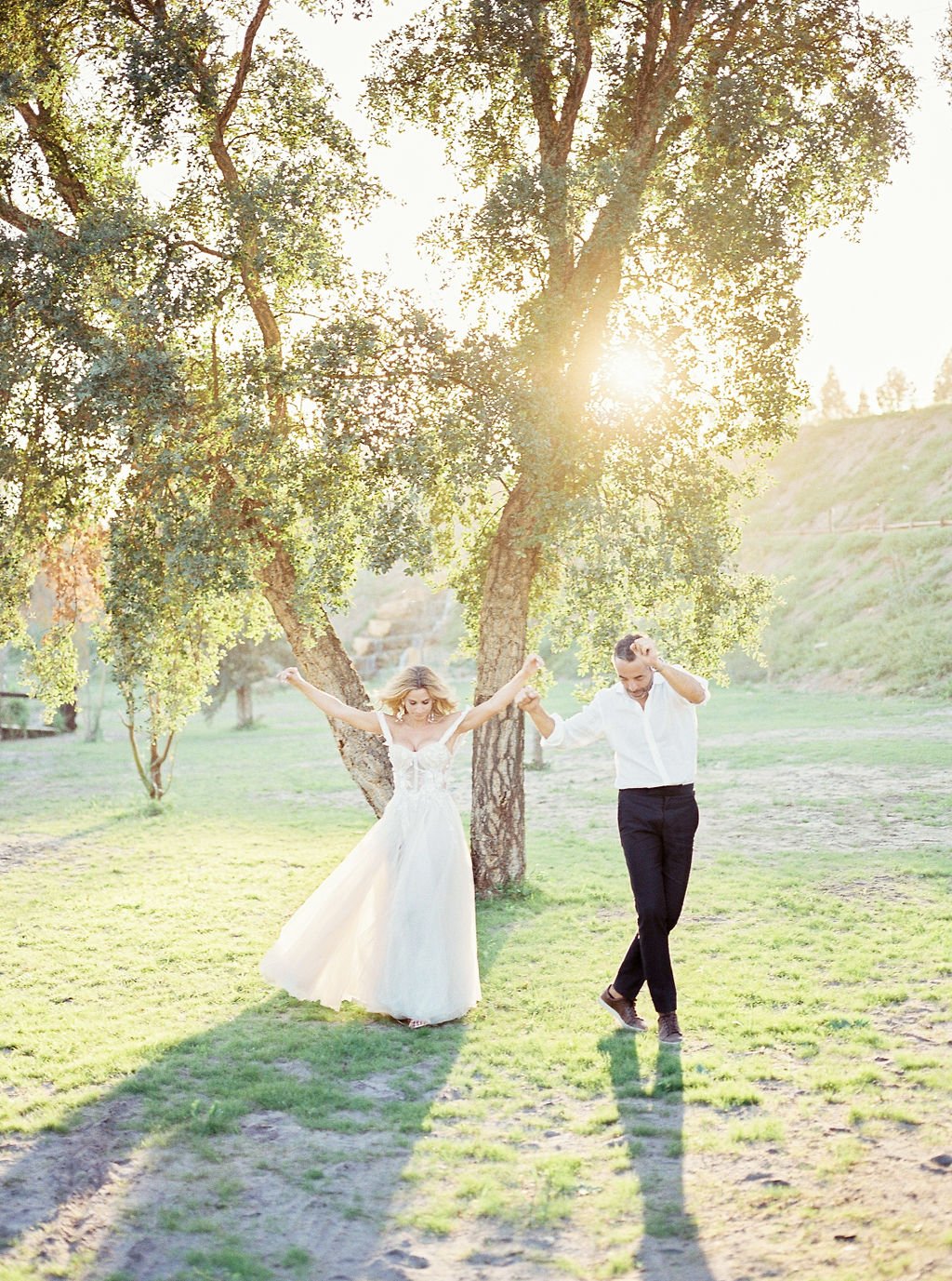 Bride and groom dancing in a garden, with a tree and the setting sun behind them