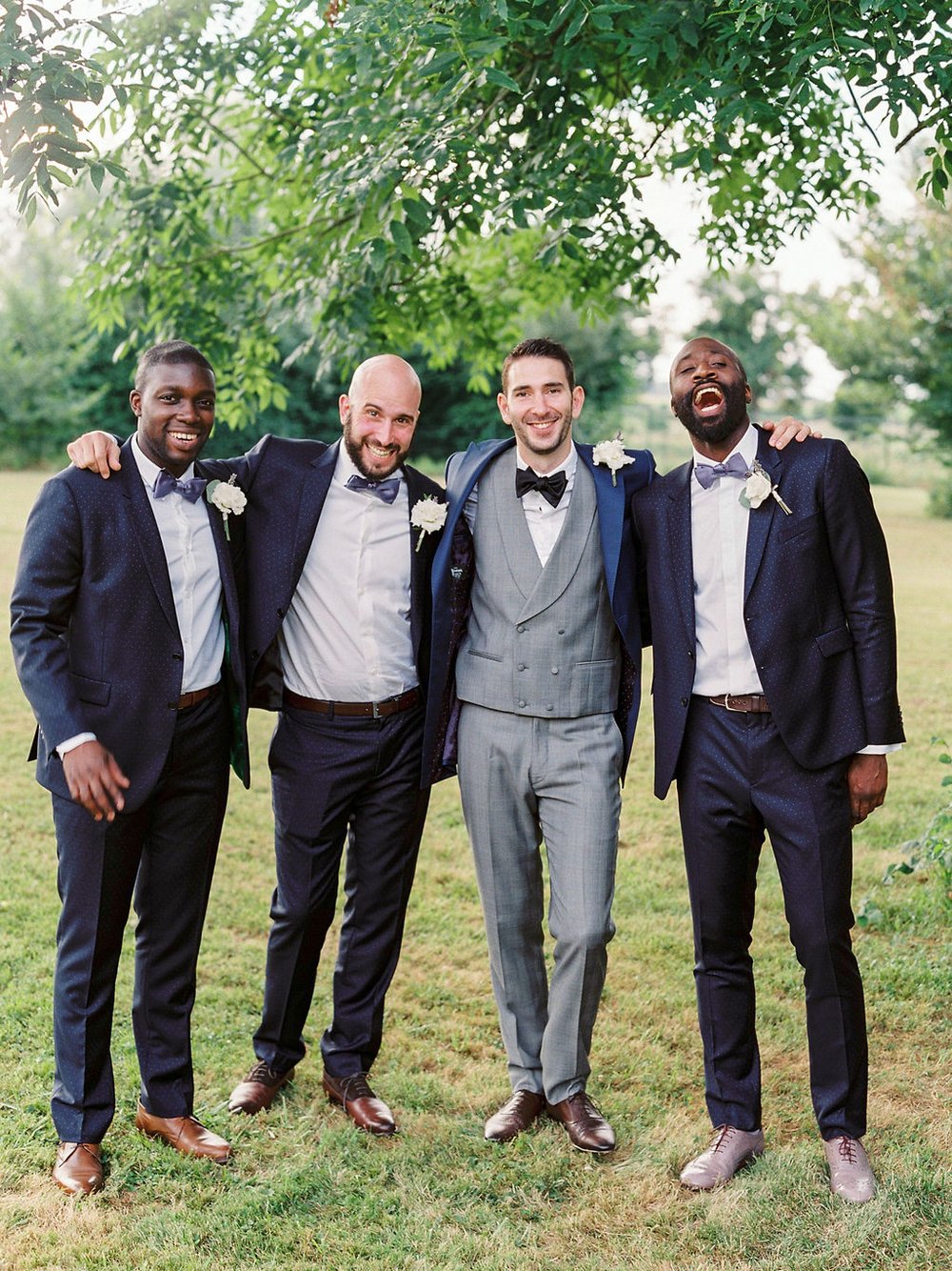 Groom and three groomsmen hugging each other's shoulders and smiling to the camera in a garden