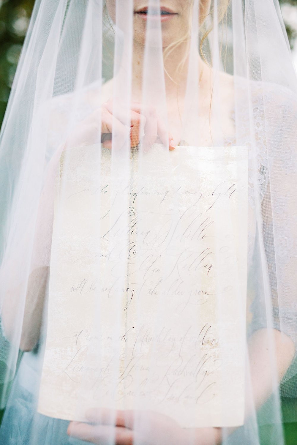An editorial image of a bride showing a written document with big calligraphy behind her veil
