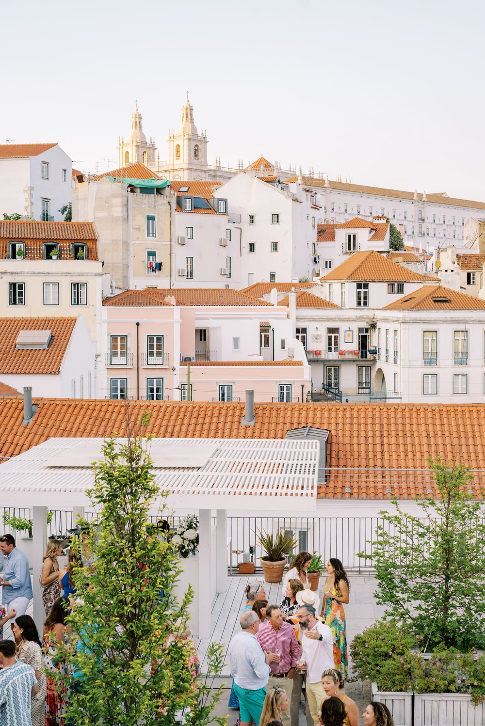 The stacked buildings in the city of Lisbon, with wedding guests drinking cocktails on the bottom and the church of Mosteiro de São Vicente de Fora on top of the photo