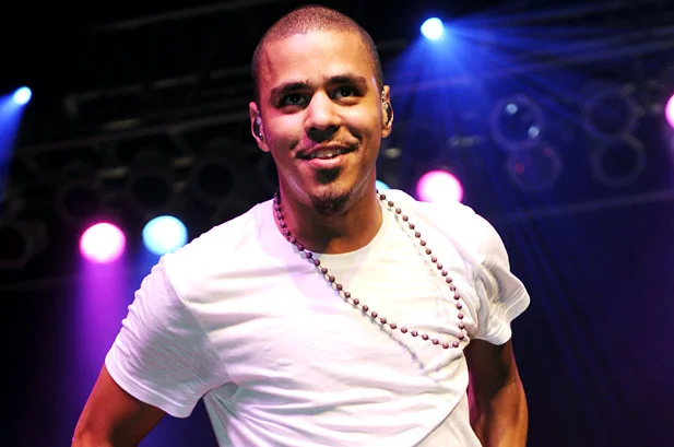 J. Cole looking extremely gorgeous in a white tee on stage as he smiles.jpg