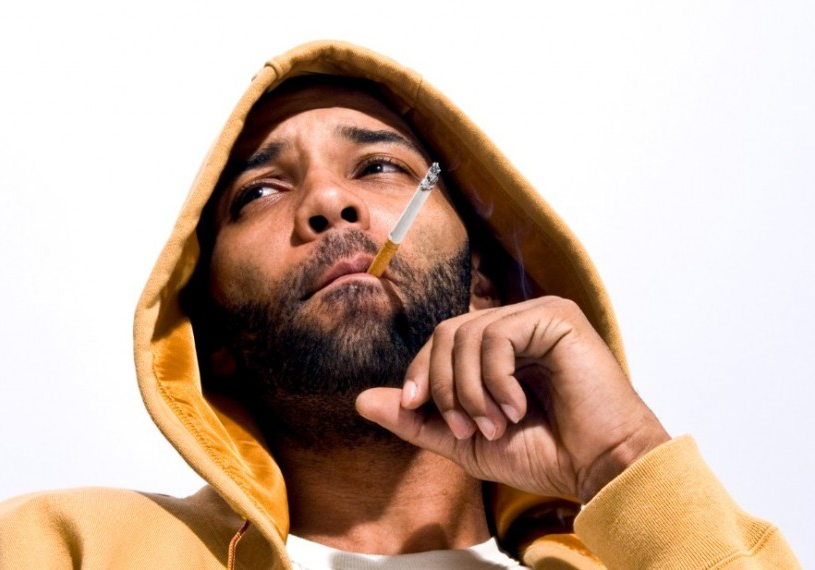 Joe Budden looking hot in a mustard yellow sweatshirt with a hood as he smokes on a cigarette that needs to be ashed asap.jpg