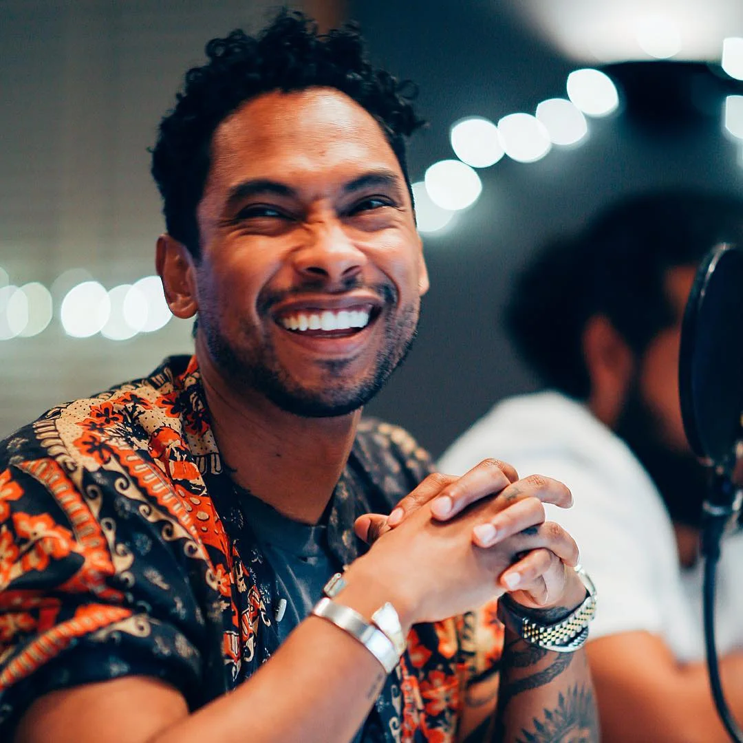 MIguel looking gorgeous as he looks off to the side and smiles with his hands closed together.jpg