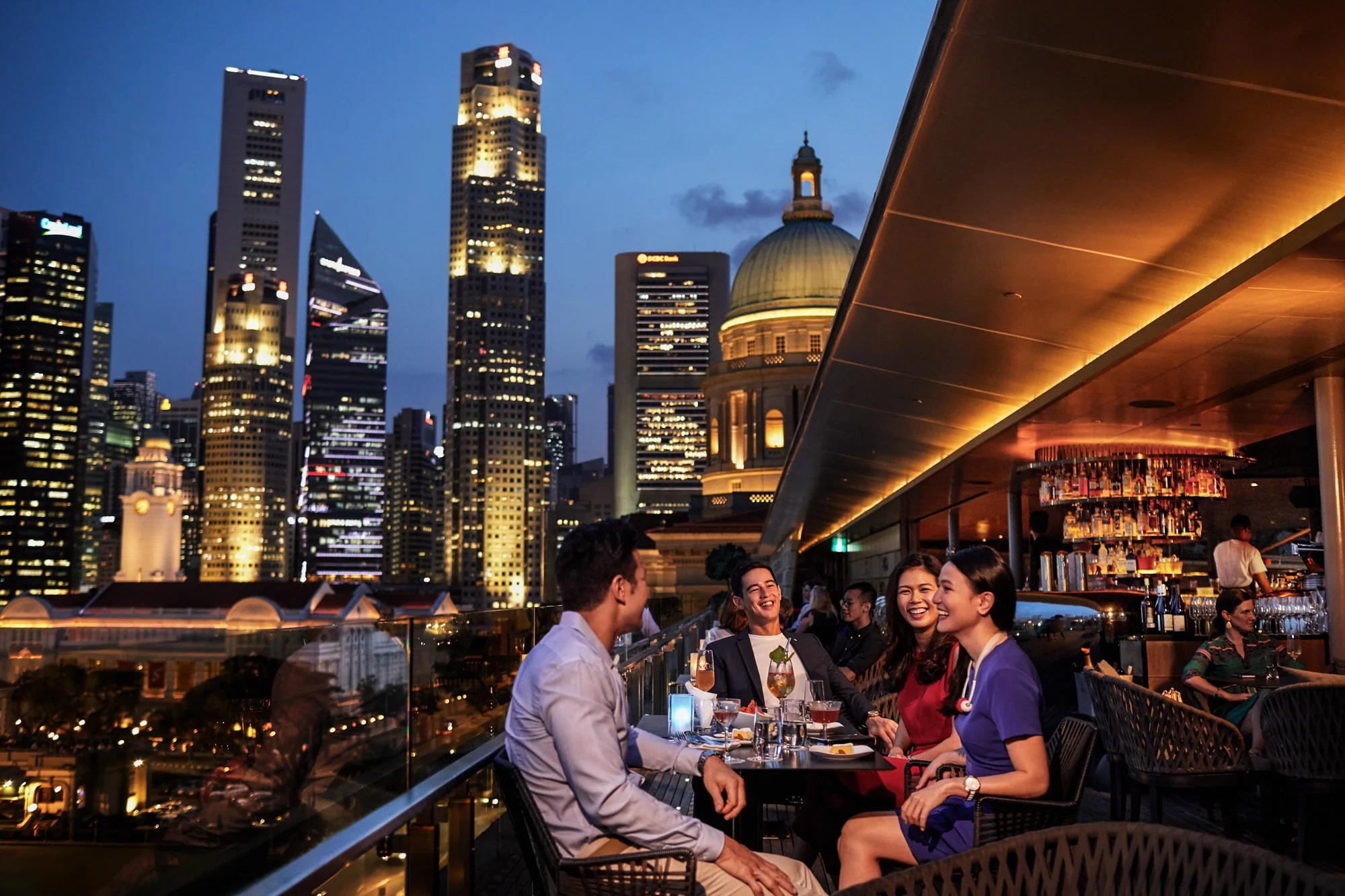 Amigos compartiendo en un rooftop con la ciudad de Singapur al fondo.