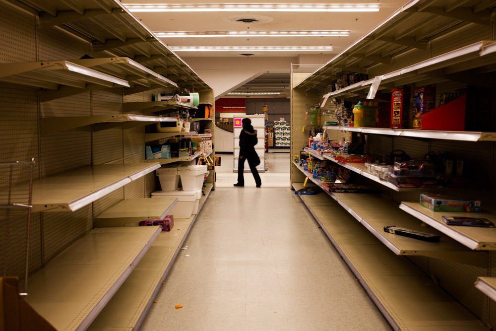 A customer wanders past an aisle that has been left with only a few items, empty packaging, and litter.