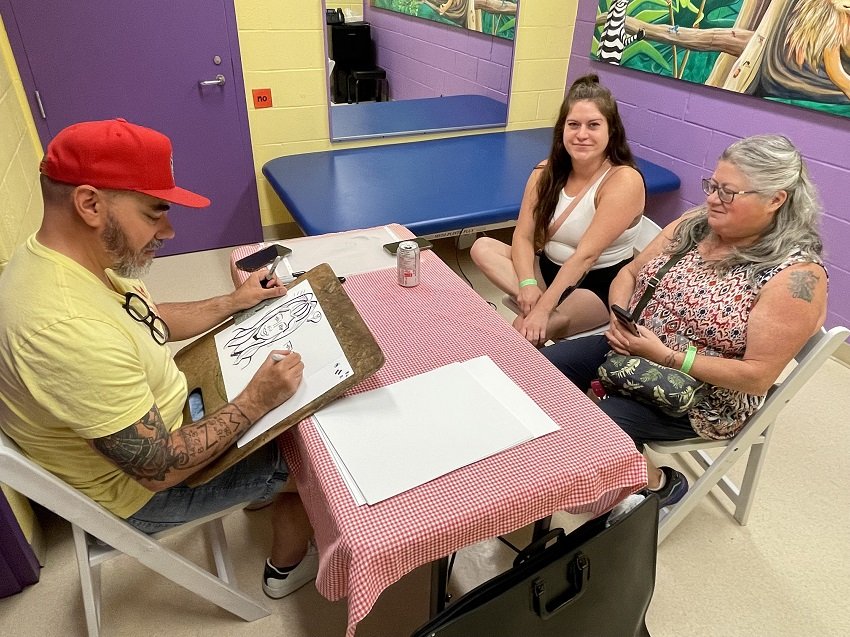  There’s an art to what caricaturist Jason Wilkins (seated at left) does, and he ably demonstrated that drawing likenesses of attendees at the Summer Social. Photo curtesy of Five Counties Kids. 