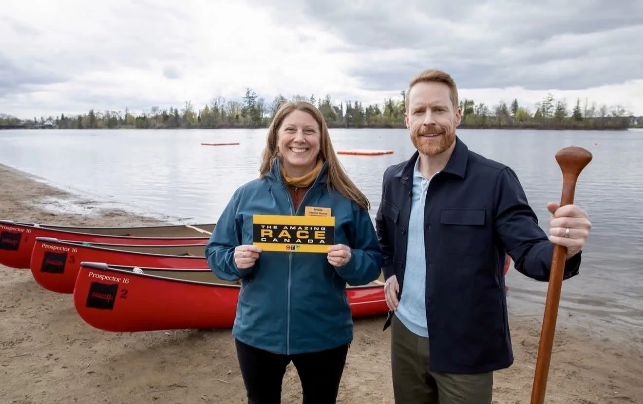 Canadian canoe museum executive director carolyn hyslop hold up a cluecard for the the amazing race canada beside host jon montgomery