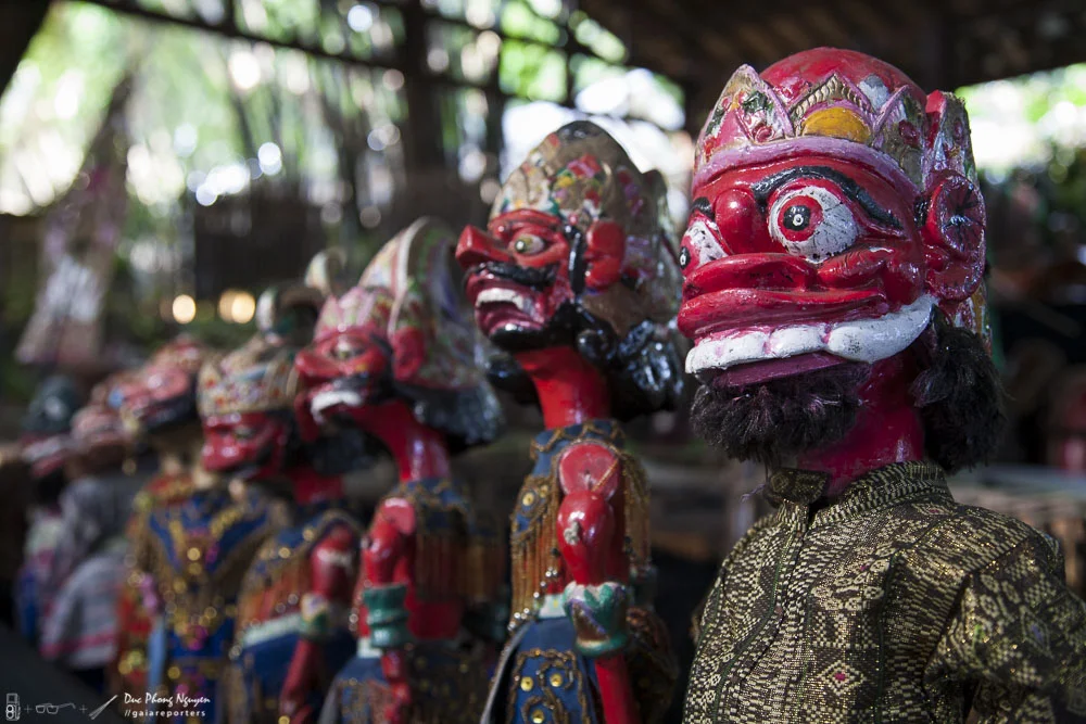 Colorful traditional Indonesian wooden masks with intricate designs, featuring exaggerated facial expressions and decorative headgear, displayed in a line.