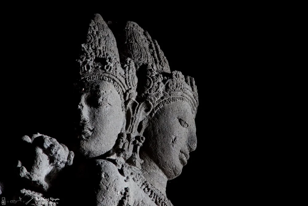Stone sculptures of three smiling female figures with intricate headdresses, illuminated against a black background.
