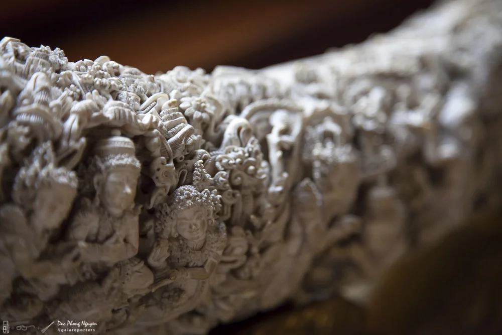 Close-up photo of an intricately carved beige or light-colored stone artifact with detailed figures and patterns.