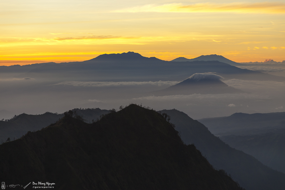 A picturesque sunrise over mountainous terrain with clouds and distant mountain peaks.