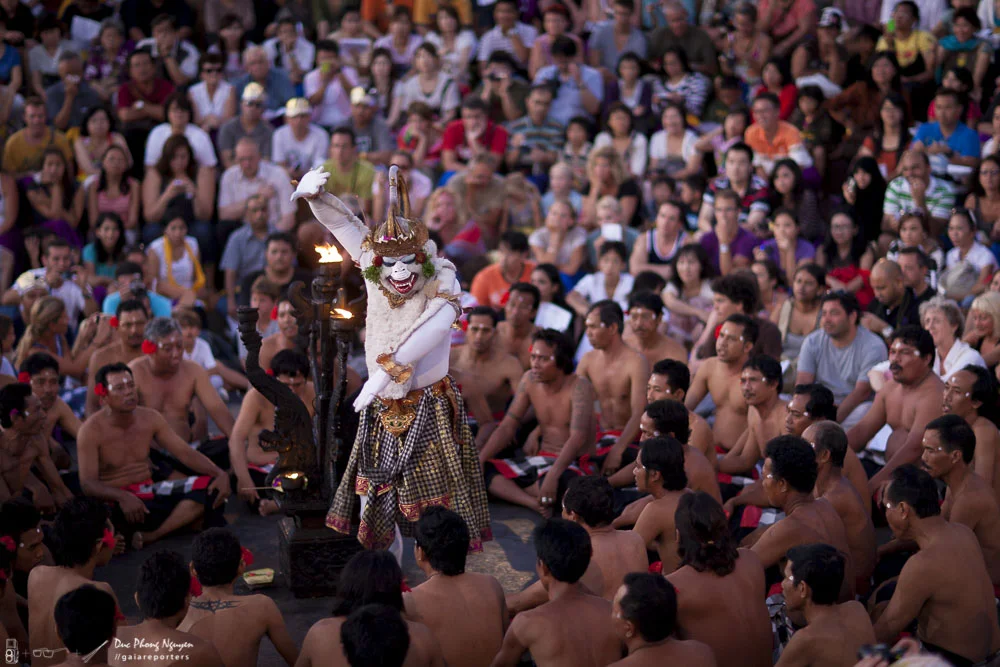 Traditional performance featuring a masked performer dressed in elaborate costume performing in front of a seated audience in an outdoor setting.