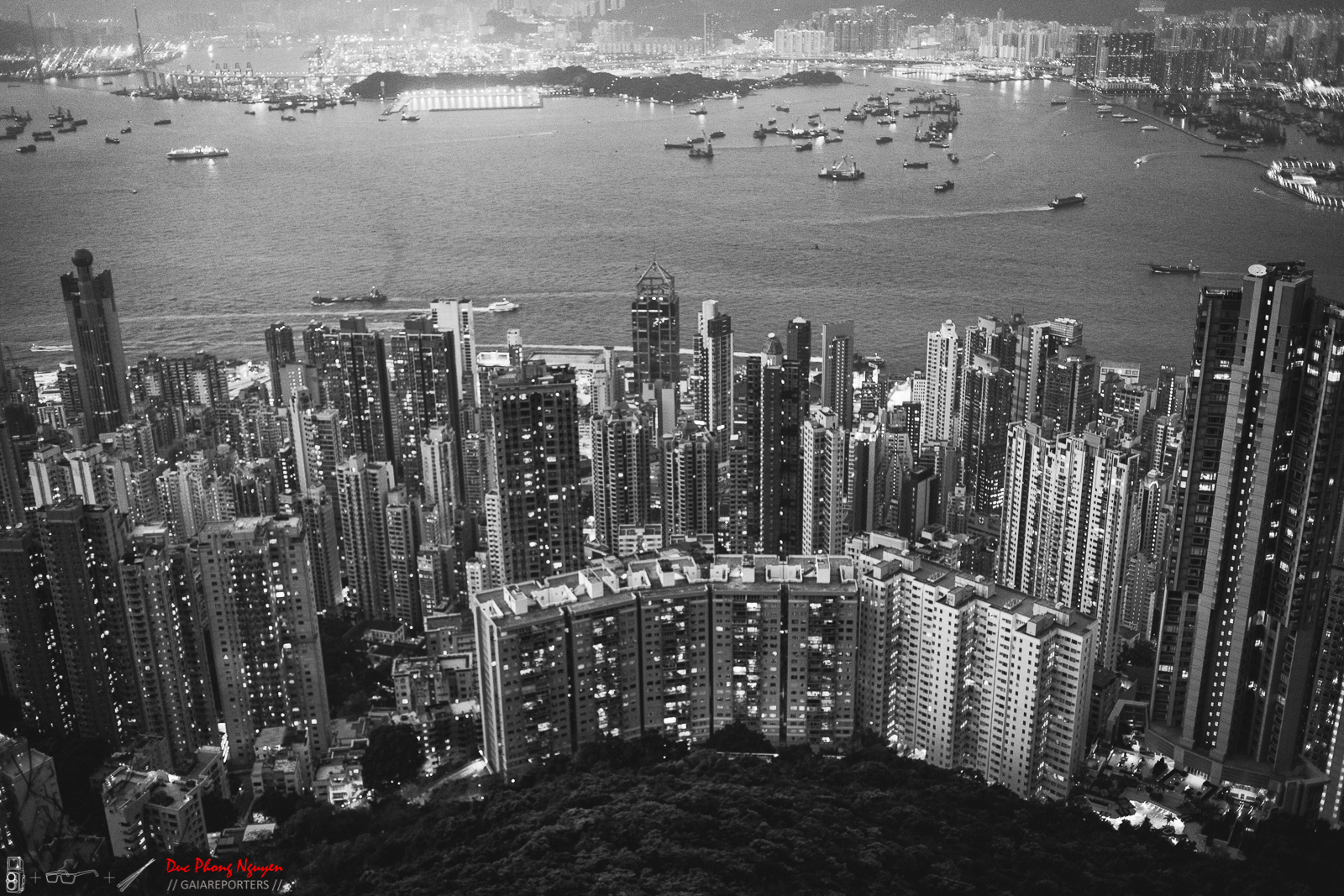 A black and white aerial view of a densely populated city with high-rise buildings and a harbor with boats and ships.
