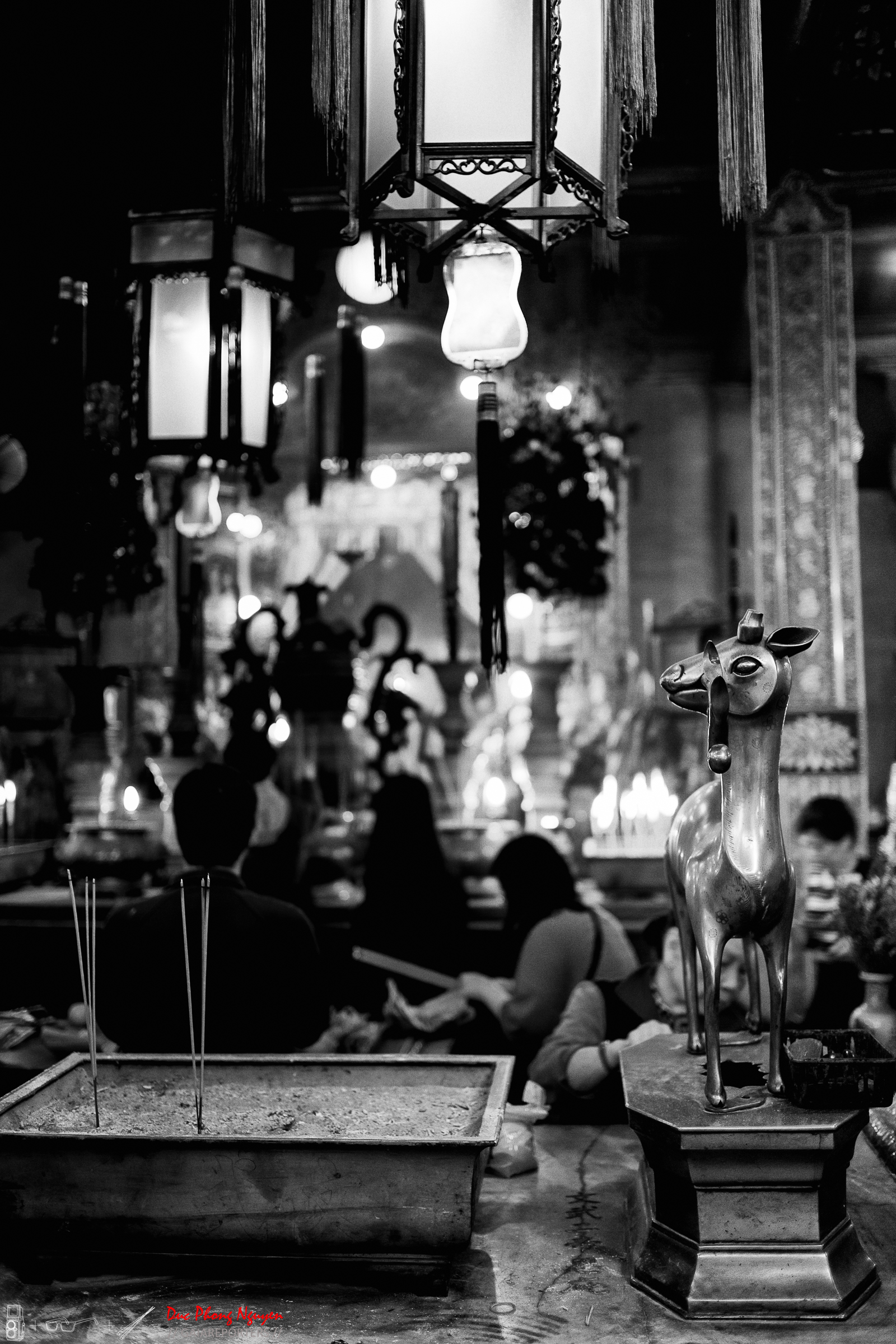 Black and white photo of an indoor restaurant or cafe with hanging lamps and people sitting at tables. A decorative sculpture of a deer is in the foreground.