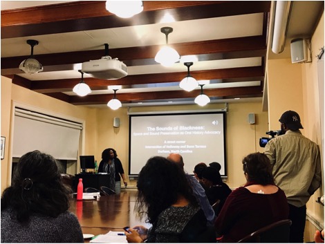 Image Description: In this photo, Nishani Frazier starts her presentation with music that is essential to the identities from her hometown. It captures one of the exciting moments from the workshop, in which Frazier enlightens her audience with captivating music and sounds to make a point of her presentation.