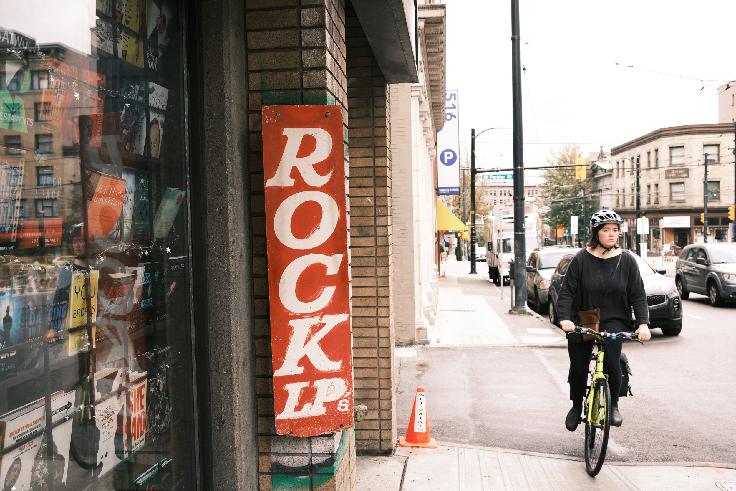 A woman cycles by book store in downtown Vancouver. Rock LPs for sale. 