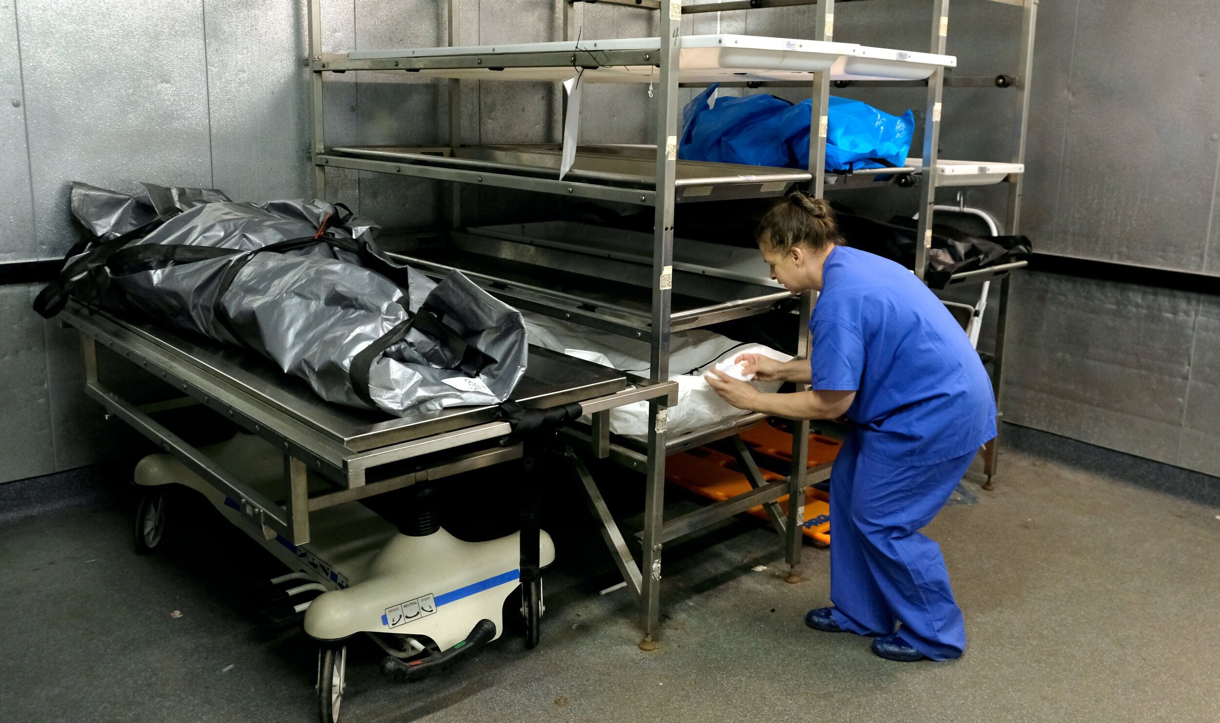  Mortician and autopsy technician Dionne Fortress checks the tag of a deceased man who tested positive for COVID-19. He is being kept in the cooler at the Lucas County Coroner's Office in Toledo. ©Toledo Blade | April 2020 