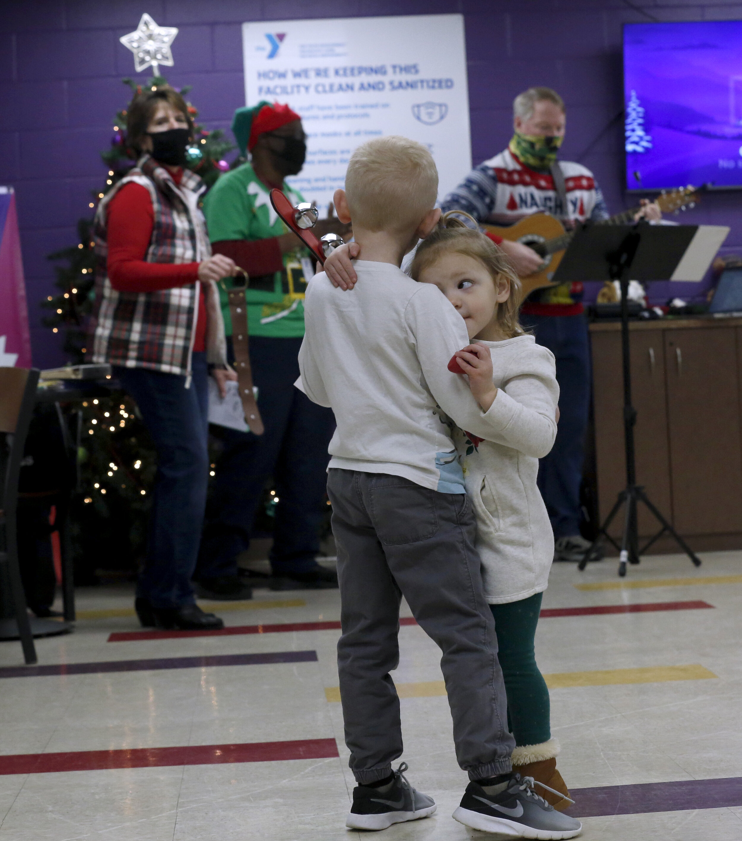  Elias Elletson, 5, and his sister Emilia, 2, hug as they play instruments to a Christmas song played by a band in the lobby of the Wolf Creek YMCA in Toledo.  © Toledo Blade | December 2020 