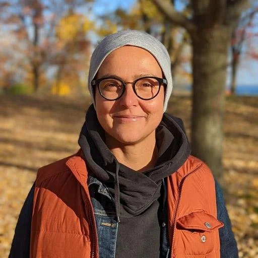 A person smiling with glasses and hat outdoors