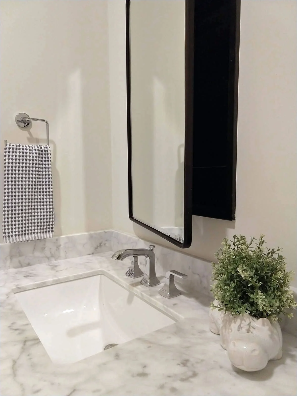 Black medicine cabinet and chrome plumbing fixtures on marble counter in bathroom remodel.