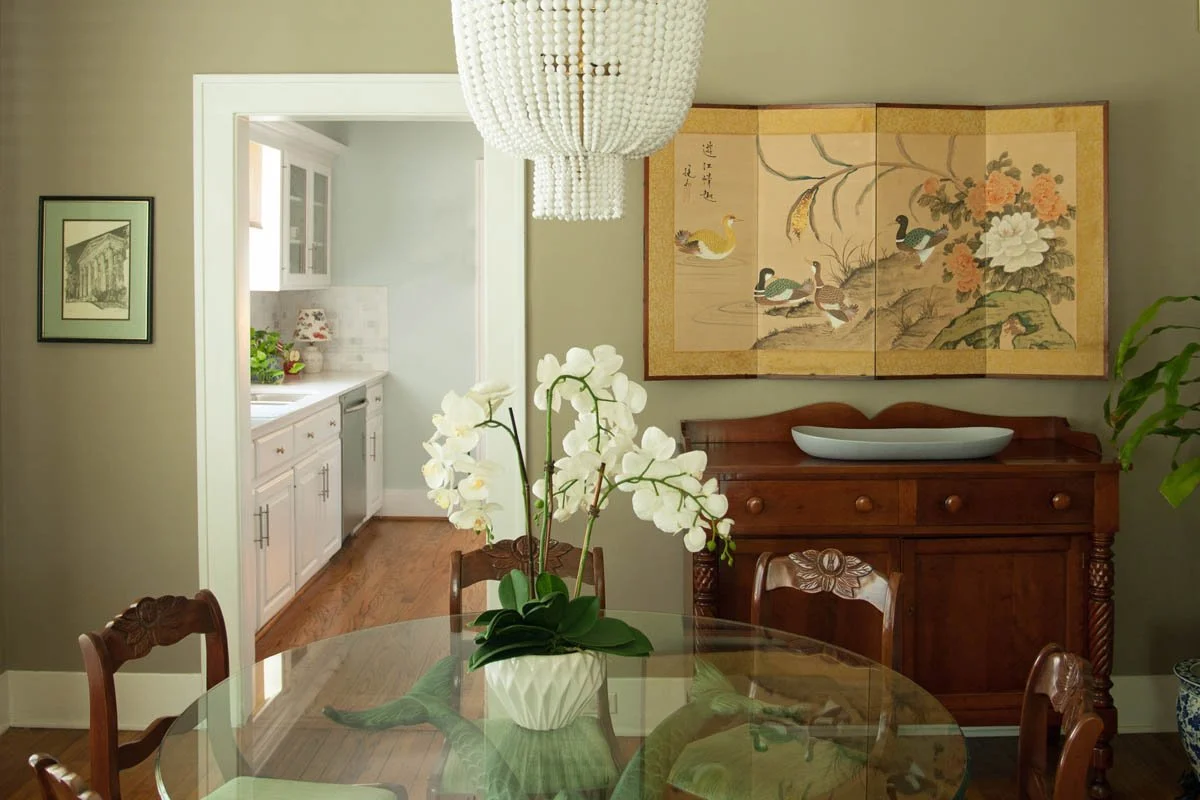 Dining room with modern lighting, a wall hung antique screen, and an antique dolphin table.