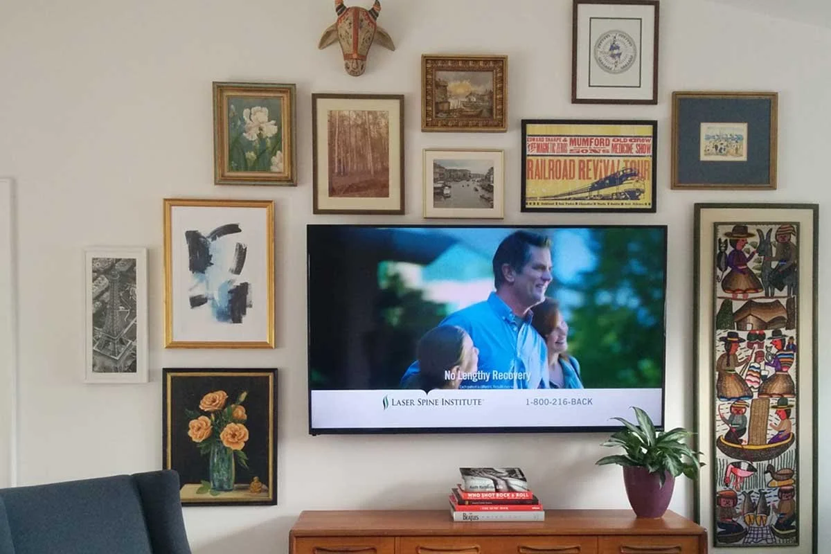 Art arranged over a TV in a loft area of a Highlands Ranch home using client's collected art.