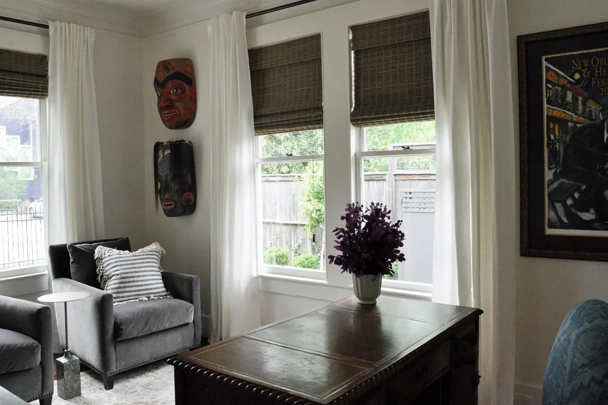 Home office with antique desk and guest seating highlighted by homeowner's art collection.