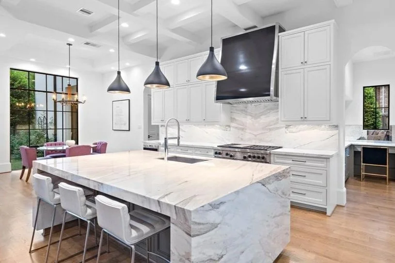 Modern kitchen with marble countertops, island, pendant lighting, and dining area with pink chairs.
