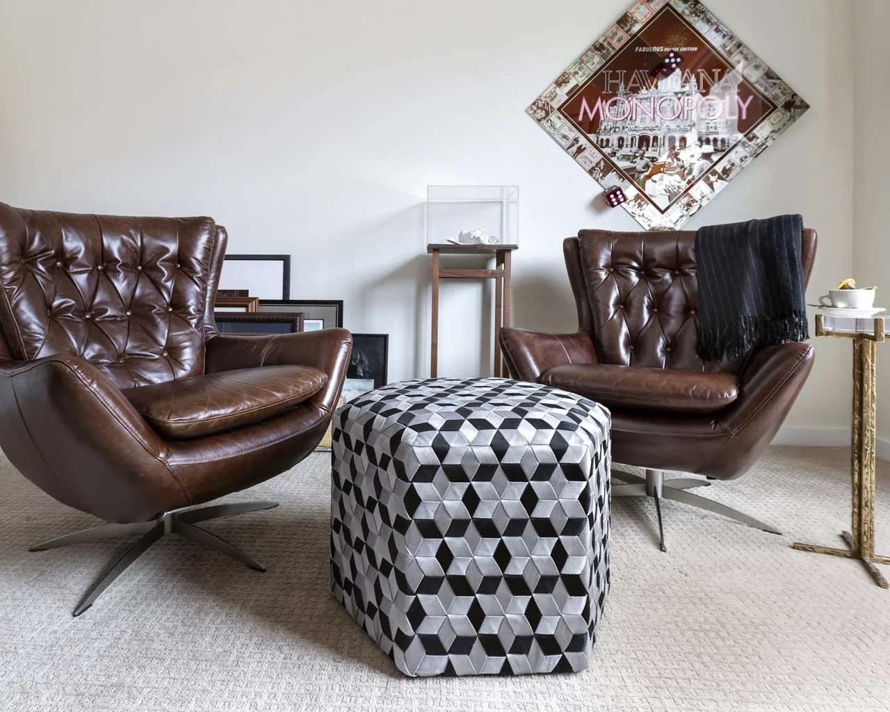 Modern living room renovation in Centennial with brown leather swivel chairs, geometric ottoman, and vintage Monopoly board wall art