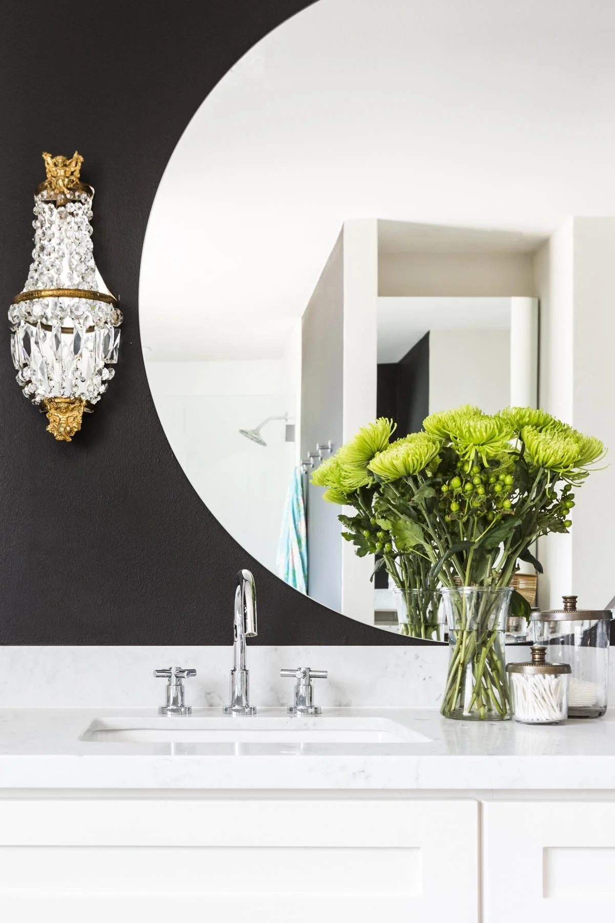 Primary bathroom vanity with custom round mirror and antique wall sconces