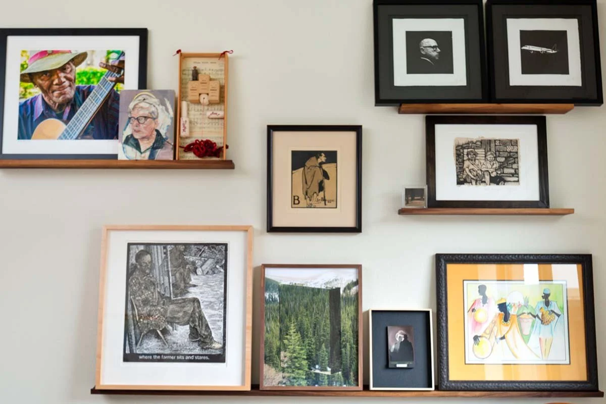 Styled shelving display with leaning framed art, handmade ceramics, sculpture, books, and collected objects arranged by interior designer