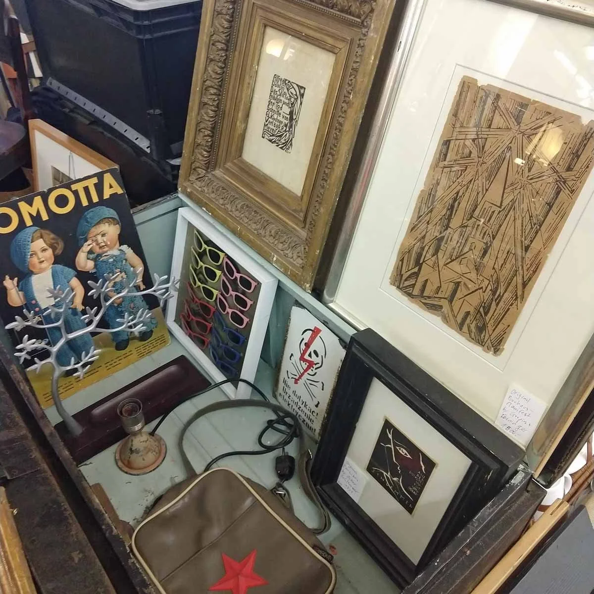 Vintage framed artwork and framed glasses displayed in an antique store, sourced for interior design project.