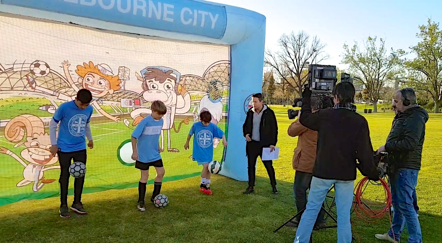 Collingwood City FC kids demonstrate soccer skills to weather presenter, Stevie Jacobs, during a live weather cross for Channel 9’s Today Show.