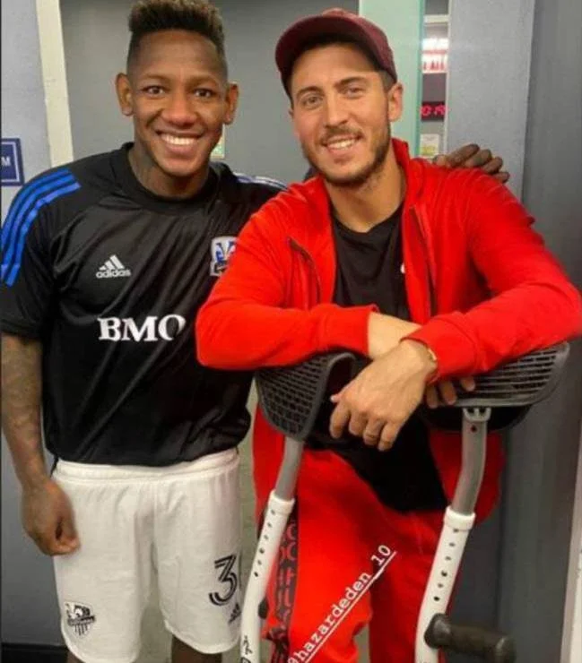 Two men smiling, one wearing a black Toronto FC soccer jersey and the other in a red hoodie, standing in a gym.