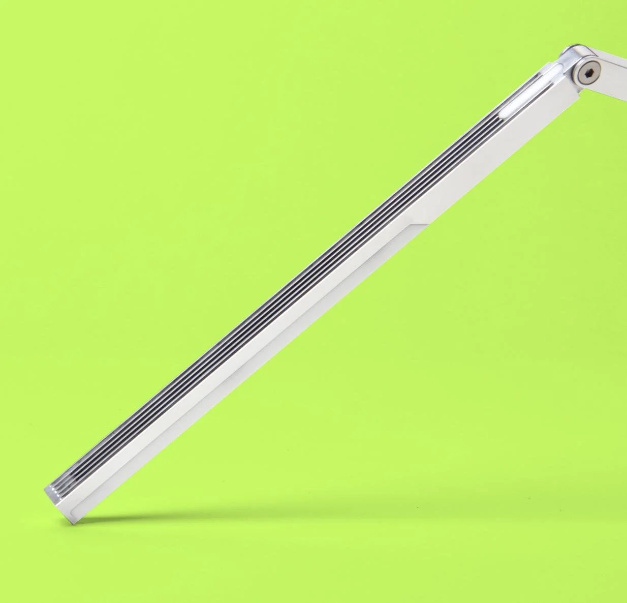 A metallic electric heater with a long, slim, rectangular shape, placed on a bright green background.