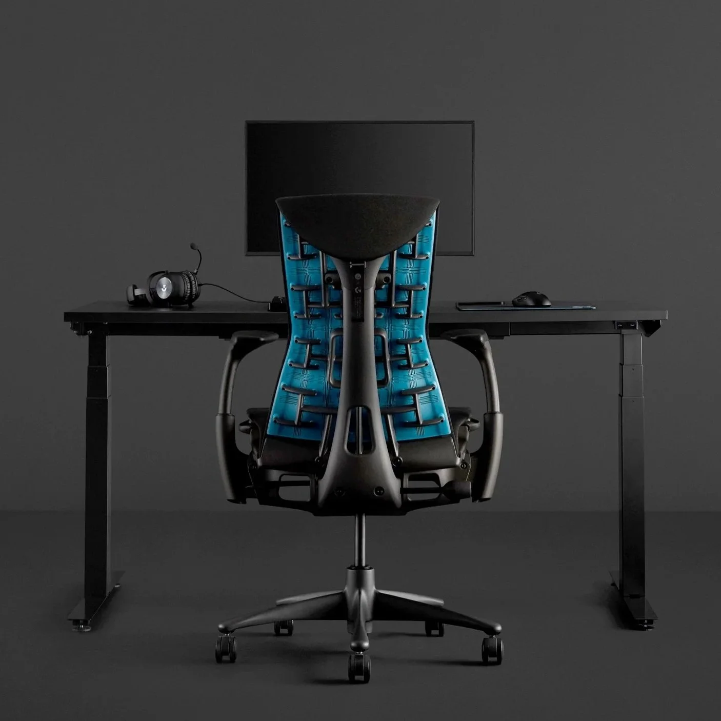 Office desk with a modern ergonomic blue and black chair, a computer monitor, a mouse, and a headset on a dark background.