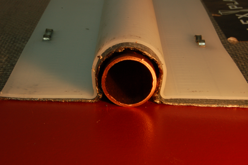 Sample #1 Graphite and stapled on polyethylene support shown taped to the substrate. The polyethylene support and the graphite sheet are significantly oversize. Where the od of the copper tube is .625", the id of the graphite sheet measures .705*, creating an air gap of maximum .040" air gap. The significantly oversize channel would prevent any installation that might provide better contact between the tube and the graphite sheet. *measurement taken with digital calipers.Click to enlarge
