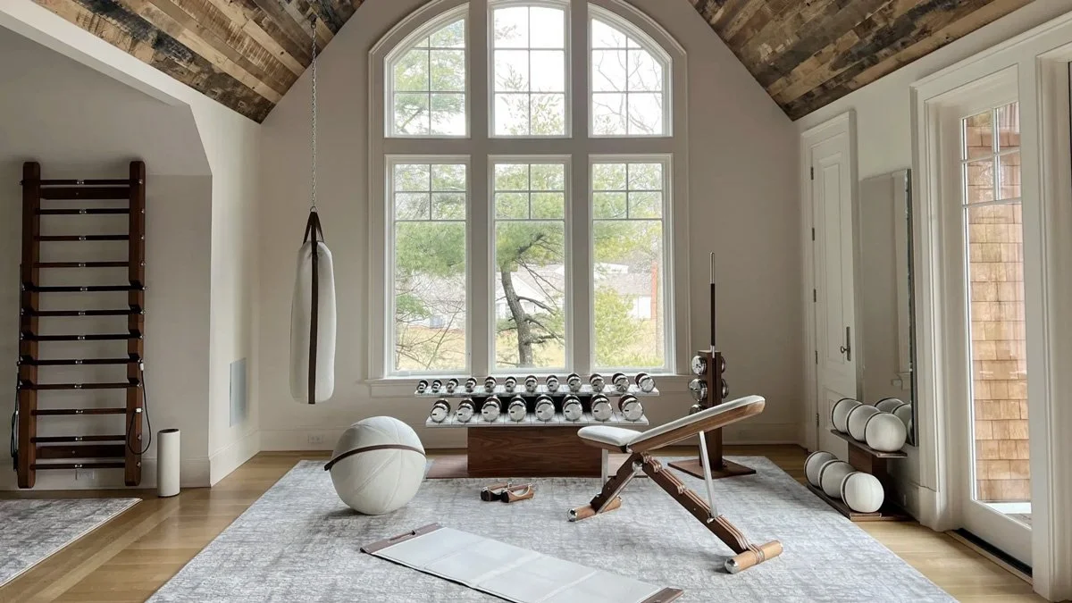 Luxury home gym with walnut wood accents, white leather PENT Fitness equipment, and natural light