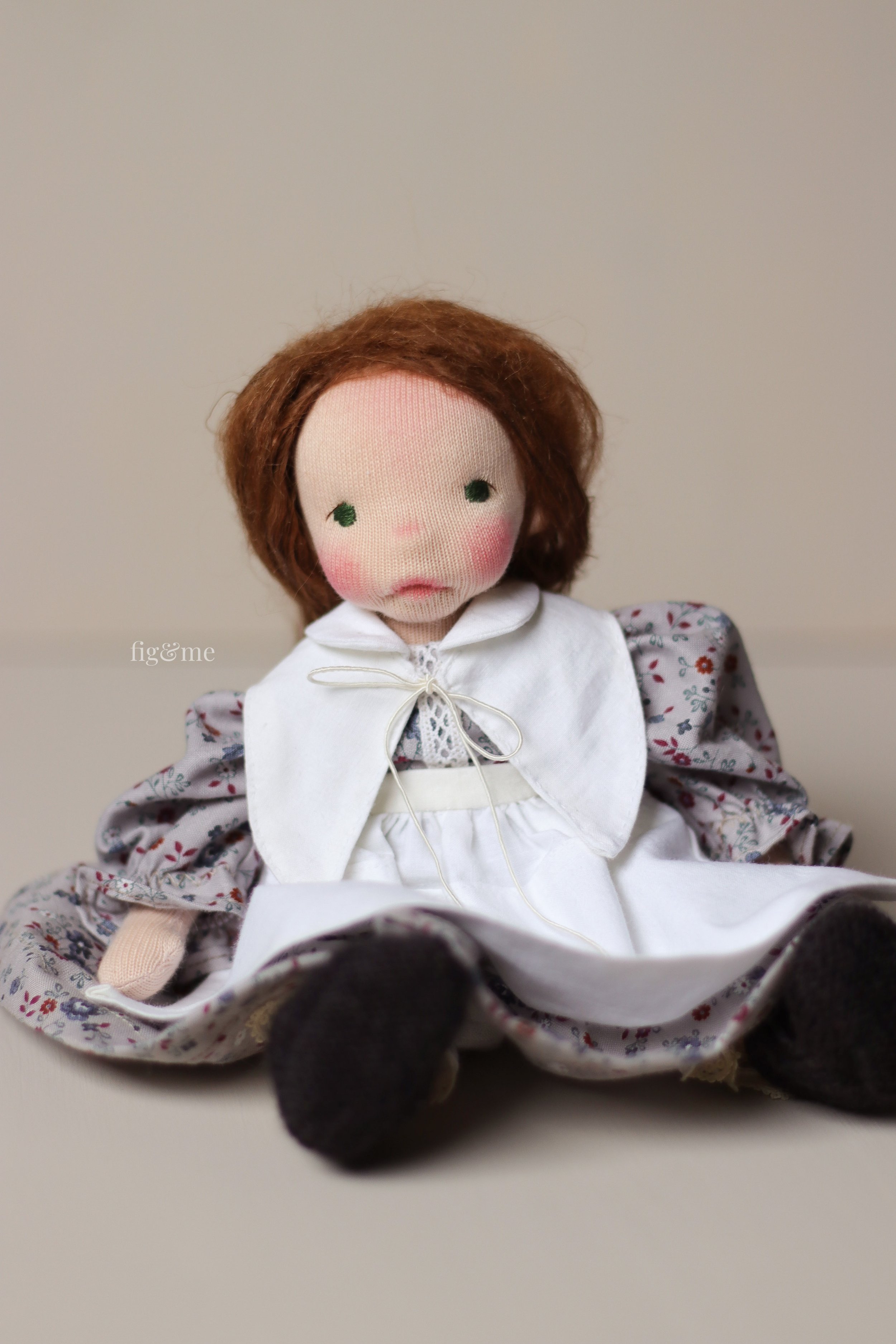 small fiber art doll with brown suri alpaca hair, green eyes, floral dress and white linen collar