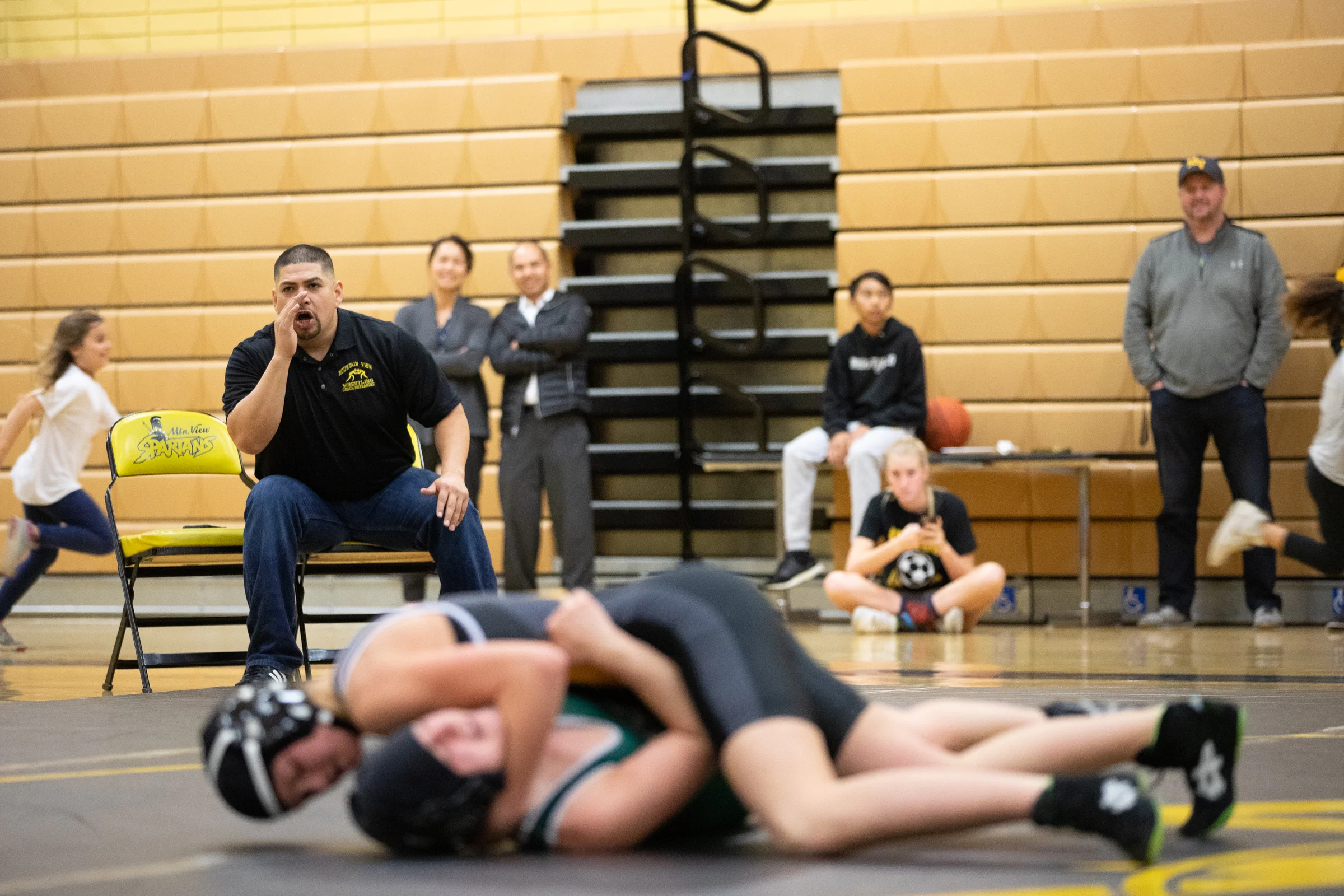 Francisco Hernandez, Mountain View High School's wrestling coach, encourages Paris Harrell during a fight against Ava Aufderheide, a student from Homestead High School, during a home meet in Mountain View, California, on Jan. 31. Seconds later, Harrell pinned Aufderheide and won her first fight of the season.
